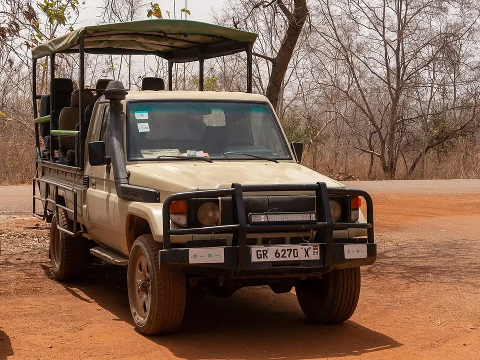 An open-sided Toyota Land Cruiser safari vehicle with a canvas roof and snorkel, parked on red earth among dry-season trees in Mole National Park
