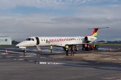 An Africa World Airlines Embraer jet on the apron at Takoradi Airport, with ground staff unloading bags