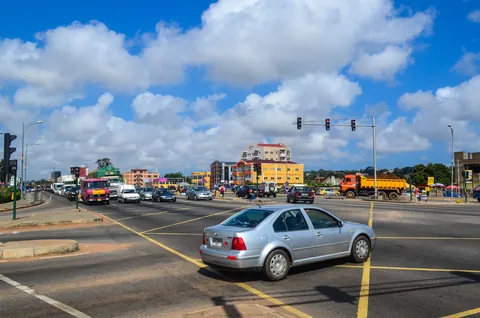 Cars, a minibus and a tipper truck at a signal-controlled junction on a highway in Accra