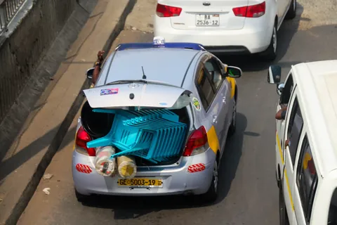 A yellow-panelled Accra taxi with its boot loaded, on the Kaneshie highway