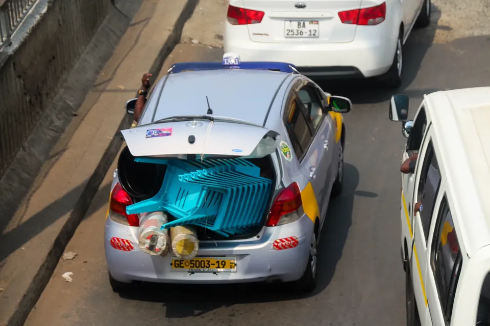 A yellow-panelled Accra taxi with its boot loaded, on the Kaneshie highway